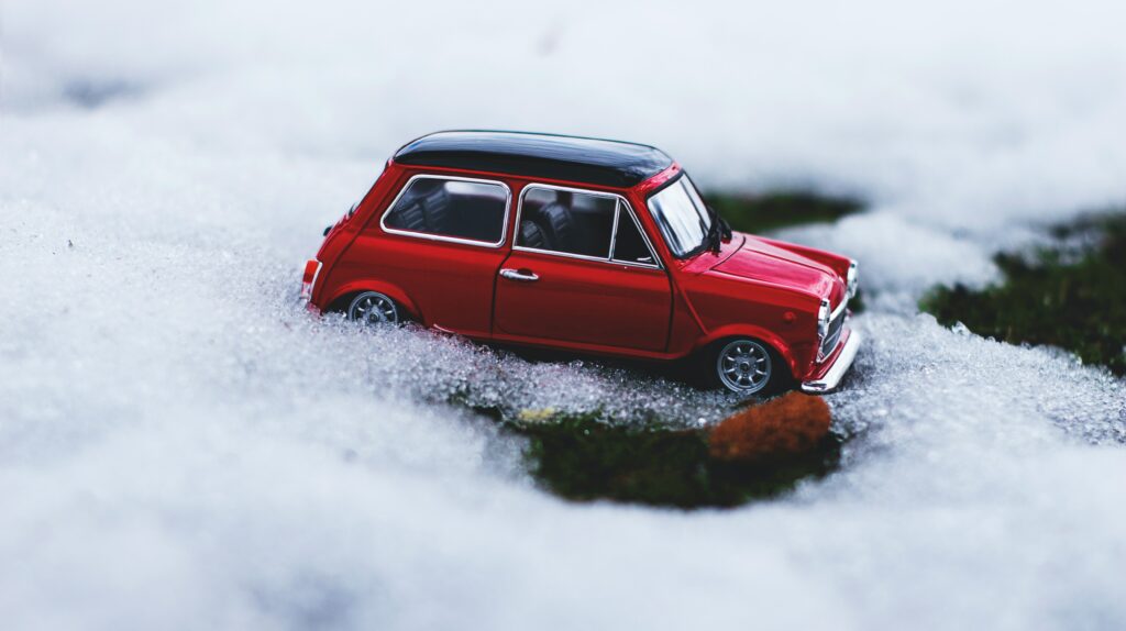Chaîne neige. Une petite voiture rouge posée sur la neige.