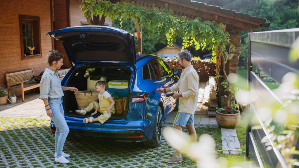 Parents organisant le coffre de voiture avec leur enfant assis à l’arrière.
